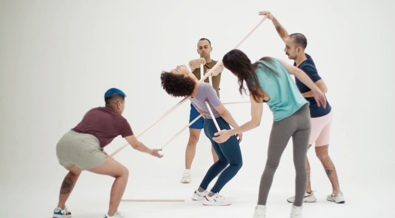 Personas interactuando con varas de madera en un espacio blanco, como parte de una performance colectiva parte de una campaña contra el odio.-Oído Odio.